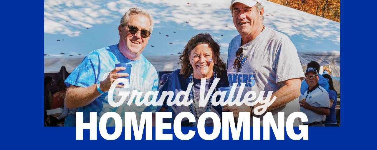 Alumni smile in front of the tailgate tent with text Grand Valley Homecoming